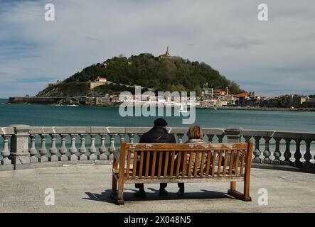 Un couple de personnes âgées se repose assis sur un banc tout en profitant du paysage devant eux, une belle île avec une grande sculpture sur le dessus Banque D'Images