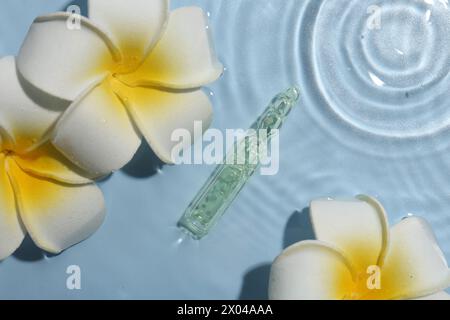 Ampoule de soin de la peau et belles fleurs de plumeria dans l'eau sur fond bleu clair, pose plate Banque D'Images