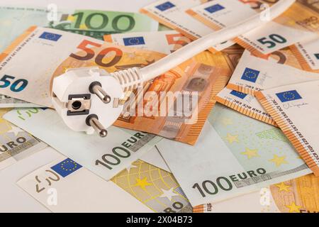 Une prise électrique blanche repose sur une table recouverte d'une grande quantité de billets en euros sur un gros plan de fond clair Banque D'Images