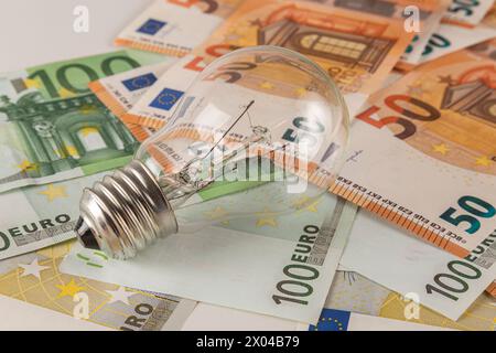 Une ampoule repose sur une table recouverte de billets en euros sur un gros plan de fond clair Banque D'Images
