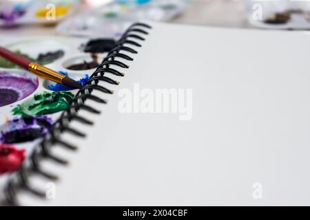 Vue rapprochée d'un cahier à reliure spirale de papier aquarelle. Peintures aquarelle floues en arrière-plan. Banque D'Images