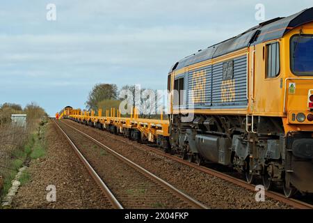 Une longue ligne de trains d'ingénierie se dresse le long d'une section vallonnée de la voie entre le passage à niveau de Sutch Lane et Burscough Bridge dans le West Lancashire. Banque D'Images