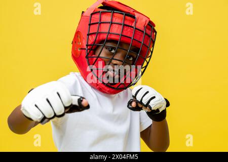 Petit garçon afro-américain combattant dans un casque de boxe de protection et des gants Banque D'Images