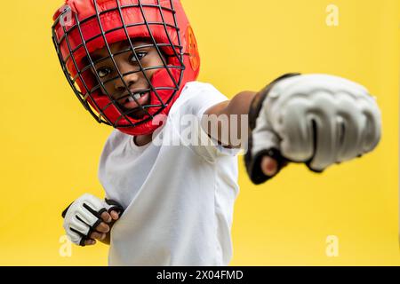 Petit garçon afro-américain combattant dans un casque de boxe de protection et des gants Banque D'Images