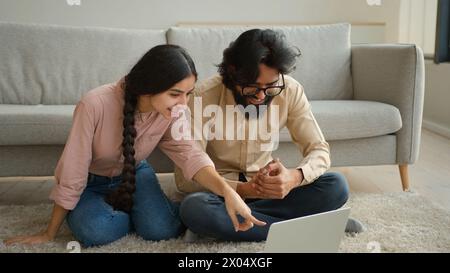 Couple multiracial homme arabe et femme indienne sur le plancher famille couple propriétaires femme petite amie et mari petit ami regardant le film portable Smart TV Banque D'Images