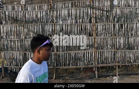 Mumbai, Maharashtra, Inde. 9 avril 2024. Un jeune homme passe devant un poisson qui est mis pour sécher au soleil sur des poteaux de bambou à une plage de Mumbai. (Crédit image : © Ashish Vaishnav/SOPA images via ZUMA Press Wire) USAGE ÉDITORIAL SEULEMENT! Non destiné à UN USAGE commercial ! Banque D'Images