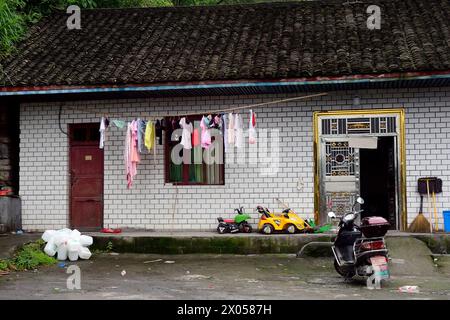 Vêtements d'enfants suspendus à sec près d'un scooter et d'une moto jouet devant une maison de cinderblock dans le Zhangjiajie, en Chine. Banque D'Images