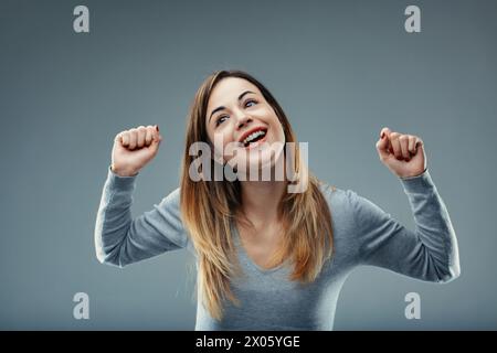 Radieuse dame célèbre le succès avec les poings levés, son sourire reflétant un moment triomphant Banque D'Images