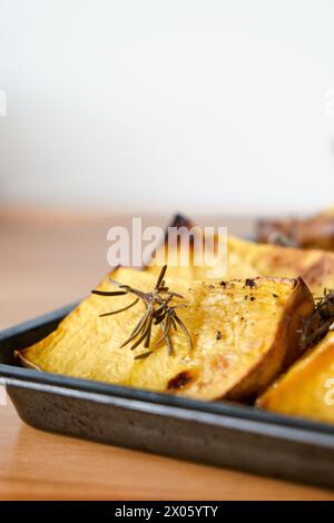 Morceaux de courge butternut rôtie au four bio sur une plaque à pâtisserie noire avec thym frais et herbes de sauge à la lumière naturelle. Banque D'Images