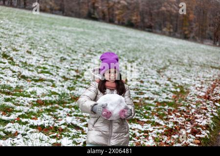 Mignonne petite fille faisant bonhomme de neige dans le parc le jour froid d'hiver Banque D'Images