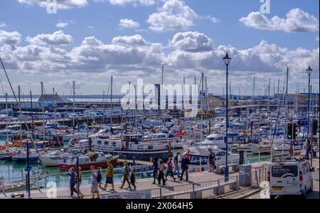 Ramsgate Royal Harbour rempli de divers bateaux et yachts, sous un ciel bleu avec des nuages blancs moelleux. Des gens marchant sur le quai. Banque D'Images