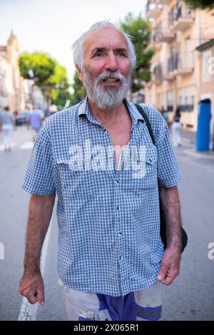 Un vieux grand-père touriste se promène autour de la station balnéaire. Un vieil homme satisfait dans une chemise profite d'une journée d'été, se promenant dans la ville. Banque D'Images