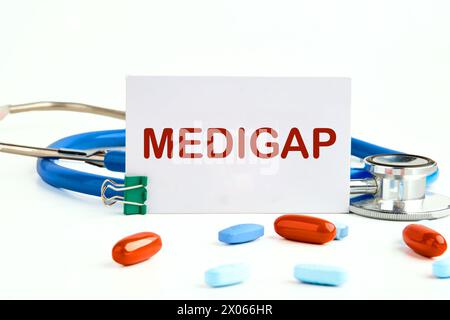 Concept médical. MEDIGAP sur une carte de visite blanche sur fond blanc à côté d'un stéthoscope et pilules, vitamines Banque D'Images