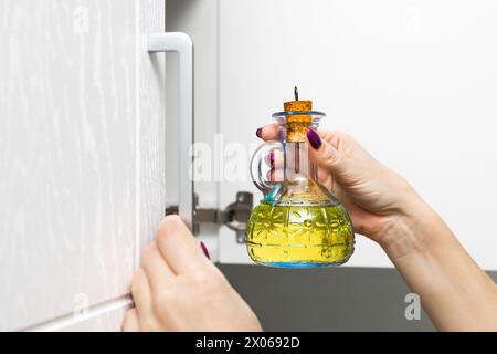 femme au foyer sort une bouteille en verre d'huile de tournesol de l'armoire de cuisine. bouteille en verre avec huile de cuisson. bouteille d'huile d'olive. homme tenant une bouteille de Banque D'Images