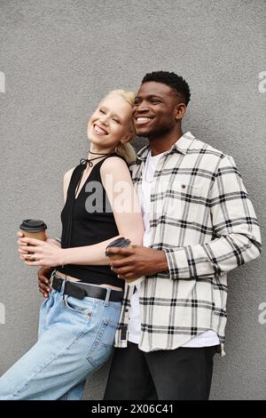 Un couple multiculturel heureux se tient côte à côte dans une rue urbaine près d’un immeuble gris. Banque D'Images