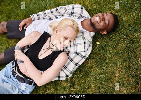 Un couple multiculturel, un homme afro-américain et une femme caucasienne, allongés sur une herbe dans un parc. Banque D'Images