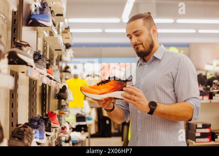 Jeune homme shopper choisissant de nouvelles baskets dans le magasin de sport moderne Banque D'Images