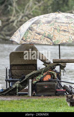 Kidderminster, Royaume-Uni. 10 avril 2024. Météo britannique : fisherman se protège de la pluie sous un gros poisson alors que des averses de pluie persistantes couvrent les Midlands aujourd'hui. Crédit : Lee Hudson/Alamy Live News Banque D'Images