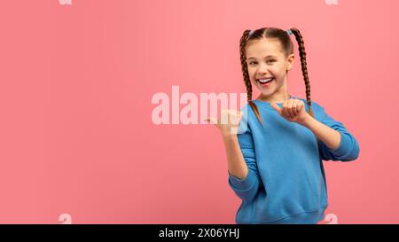 Fille heureuse pointant à l'espace sur fond rose Banque D'Images