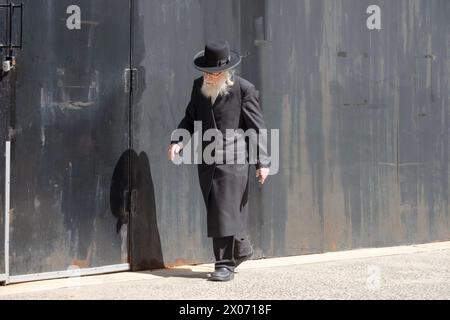 Un homme juif hassidique plus âgé marche sur un fond de bois vert. À Williamsburg, Brooklyn, New York. Banque D'Images