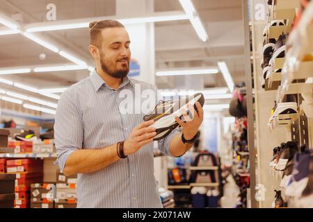 Jeune homme acheteur choisissant de nouvelles baskets pour courir au magasin de sport moderne Banque D'Images