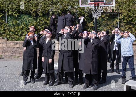 Un groupe de garçons juifs orthodoxes regarde l'éclipse solaire de 2024 depuis la cour d'école de leur école paroissiale. Dans le comté de Rockland, New York. Banque D'Images