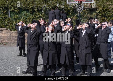 Un groupe de garçons juifs orthodoxes regarde l'éclipse solaire de 2024 depuis la cour d'école de leur école paroissiale. Dans le comté de Rockland, New York. Banque D'Images