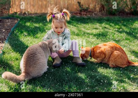 Belle petite fille avec des chats dans le jardin arrière de printemps Banque D'Images