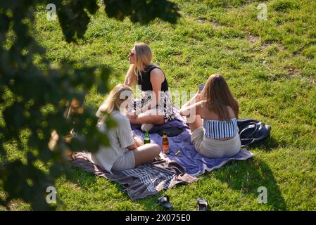 Jeunes femmes copines traînant boire de la bière socialisant et parlant assis sur une couverture dans un parc public à Gdansk, Pologne, Europe, UE Banque D'Images