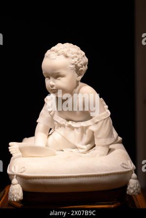 Statue en marbre de bébé garçon dans une robe assise sur un coussin Banque D'Images