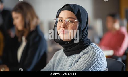 Beau portrait d'une femme musulmane multiethnique portant Hijab et lunettes, souriant charmante et posant à la caméra. Heureux diversifié jeune femme dans des vêtements décontractés à l'intérieur. Banque D'Images