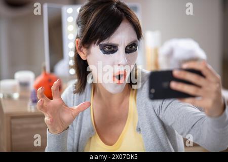 femme excitée dans le maquillage clown lumineux d'halloween prenant un selfie Banque D'Images