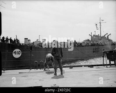 LIBÉRATION DE L'EUROPE : LES PRISONNIERS ALLEMANDS ARRIVENT EN ANGLETERRE DE NORMANDIE. 12 JUIN 1944, QUAIS DE SOUTHAMPTON. PRISONNIERS ALLEMANDS, SOLDATS, MARINS, AVIATEURS ET CIVILS ARRIVANT DE FRANCE DANS LES PORTS BRITANNIQUES. - Un prisonnier allemand fait une pause de son travail de peinture pour regarder un LCT chargé de matériel de guerre quitter le port britannique pour la tête de pont en Normandie Banque D'Images