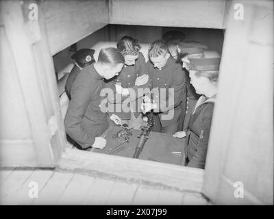 YACHT D'INSTRUCTION DEMS MOBILE. 23 FÉVRIER 1942, À BORD DU MY MELITA, BAIE DE GOUROCK. LE LANCEMENT MOTORISÉ EST LE PREMIER LANCEMENT INSTRUCTIF À ÊTRE UTILISÉ POUR L'ÉQUIPEMENT DÉFENSIF DES NAVIRES MARCHANDS AU ROYAUME-UNI. IL EFFECTUE DES TRAJETS QUOTIDIENS JUSQU'AUX MOUILLAGES POUR TENIR LES MARINS MARCHANDS INFORMÉS ET INSTRUITS DES DERNIÈRES AMÉLIORATIONS POUR LA DÉFENSE DE LEURS NAVIRES. - Une classe de marins marchands apprend à démonter le pistolet Hotchkiss dans la cabine de MA MELITA Banque D'Images