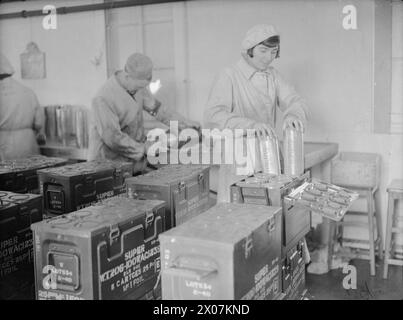 PRODUCTION DE MUNITIONS EN GRANDE-BRETAGNE, 1940 - Une travailleuse de munitions emballe des cartouches dans ses boîtes de transport dans une usine de munitions, quelque part en Grande-Bretagne. Derrière elle, deux autres ouvriers peuvent être vus Banque D'Images