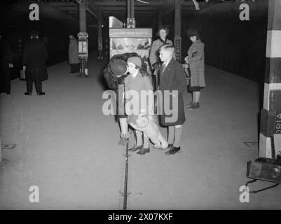 LES CARTER EN TEMPS DE GUERRE : LA VIE QUOTIDIENNE POUR Une FAMILLE BRITANNIQUE SUR LE FRONT INTÉRIEUR, ANGLETERRE, C 1940 - Mme carter embrasse sa fille Angela au revoir sur le quai de Hayward's Heath station. Mme carter a passé la journée avec ses enfants évacués Angela et Michael (debout à côté d'eux, à droite) dans leur foyer d'accueil. Angela est contrariée à l'idée que sa mère part et tient fermement à la jambe de son grand ours en peluche Banque D'Images