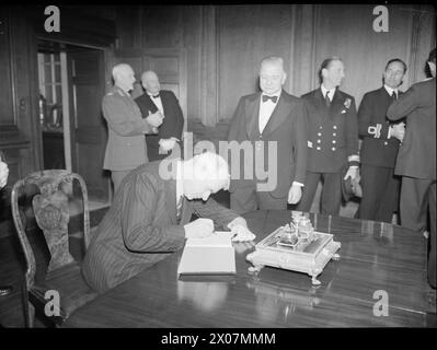 DÎNER DU CONSEIL D'ADMINISTRATION DE L'AMIRAUTÉ AUX PREMIERS MINISTRES DE L'EMPIRE. 8 MAI 1944, DANS LE PAINTED HALL DU ROYAL NAVAL COLLEGE GREENWICH. LE DÎNER ÉTAIT EN L'HONNEUR DES PREMIERS MINISTRES DE L'AUSTRALIE, DU CANADA, DE L'AFRIQUE DU SUD ET DE LA NOUVELLE-ZÉLANDE, ET ÉTAIT PRÉSIDÉ PAR LE PREMIER LORD DE L'AMIRAUTÉ, M. A. V ALEXANDER. - M. Peter Fraser, premier ministre de Nouvelle-Zélande, signe le livre de visite à son arrivée au Royal Naval College, sous la surveillance de M. A. V Alexander Banque D'Images