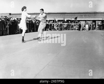 CAMP DE VACANCES REPREND : LA VIE QUOTIDIENNE DANS UN CAMP DE VACANCES DE BUTLIN, FILEY, YORKSHIRE, ANGLETERRE, ROYAUME-UNI, 1945 - les couples prennent un tour sur la patinoire à patin à roulettes au camp de vacances de Butlin, Filey, tandis que la foule se tient autour du bord au soleil, regardant l'action Banque D'Images