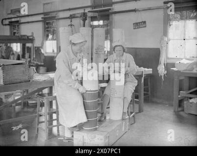 THE WOMEN BEHIND THE GUNS : MUNITIONS PRODUCTION IN BRITAIN, 1940 - deux femmes composent une charge cordite dans une usine d'armes, quelque part en Grande-Bretagne Banque D'Images