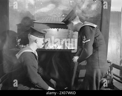 HOME FLEET CHRISTMAS : SHIPWRIGHTS CONSTRUISENT LE MODÈLE DE LA NATIVITÉ POUR LA CHAPELLE DU NAVIRE. 24 DÉCEMBRE 1942, À BORD DU HMS DUNLUCE CASTLE, DE LA FLOTTE LOCALE. - Marins avec la scène miniature représentant la naissance du Christ dans la chapelle du navire Banque D'Images