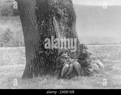 COLONIE POUR ARTISTES DE MOINS DE SIX ANS : ÉVACUÉS À DARTINGTON HALL, TOTNES, DEVON, ANGLETERRE, 1941. - Eileen Earles (7 ans) et Doreen Hogwood (6 ans) profitent du soleil, assis ensemble sur l'herbe sous un arbre, lors d'une pause de cours à Dartington Hall, Devon Banque D'Images