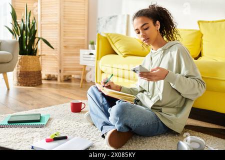 Une jeune femme avec un cahier et un stylo est assise sur le sol absorbée par la pensée, entourée par les outils de l'inspiration. Banque D'Images