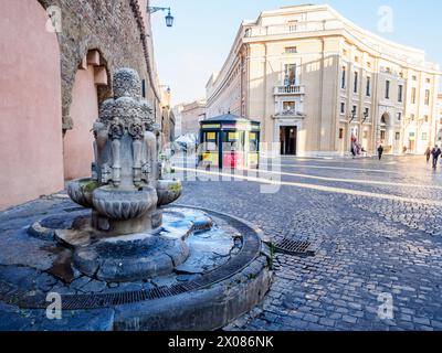 La Fontana delle Tiare est située sur le pavé de largo del Colonnato, à droite de l'arcade ouverte en 1933 le long des murs du Passetto. La fontaine a été construite en travertin par Pietro Lombardi en 1927. Sur une base tripartite robuste, il y a trois plateaux en forme de coquille semi-circulaire qui collectent l'eau versée par trois paires de becs, placés sur la tête des clés de Saint-Pierre et surmontés par trois tiaras papal sur lesquels un autre de couronnement: Les armoiries de Rome et celle du quartier Borgo sont sculptées dans les espaces entre les clés - Rome, Italie Banque D'Images