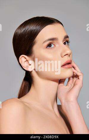 Une jeune femme brune avec une queue de cheval frappe une pose exsudant élégance et confiance dans un cadre de studio sur un fond gris. Banque D'Images