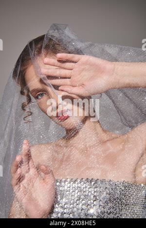 Une jeune femme prend la pose dans un studio, vêtue d'une robe de mariée avec un voile qui coule gracieusement sur sa tête. Banque D'Images