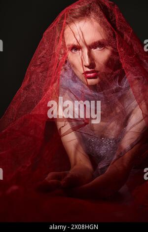 Une jeune femme respire la beauté classique dans un magnifique voile rouge et robe, frappant une pose dans un cadre de studio sur un fond noir. Banque D'Images