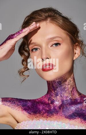 Une jeune femme à la beauté classique pose dans un studio recouvert de peinture violette et rose, dégageant une élégance éthérée. Banque D'Images