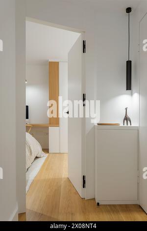 Intérieur moderne de la chambre à coucher aperçu à travers une porte entrouverte avec mobilier minimaliste et éclairage doux Banque D'Images