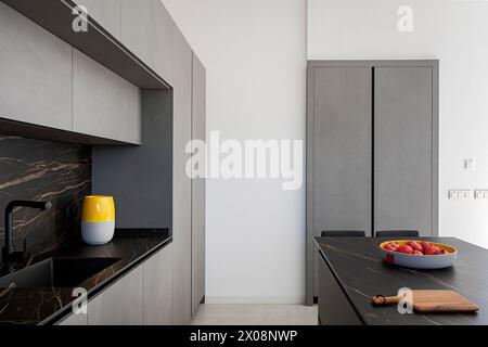 Intérieur de cuisine moderne aux lignes épurées, avec des comptoirs en marbre foncé, des armoires grises et une touche de couleur avec un vase jaune Banque D'Images
