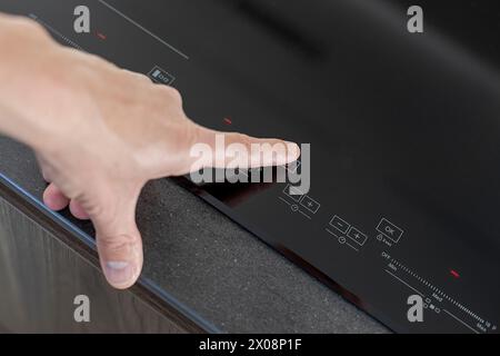 Une personne anonyme ajuste les réglages sur une cuisinière à induction élégante, mettant en valeur la technologie de cuisine moderne Banque D'Images